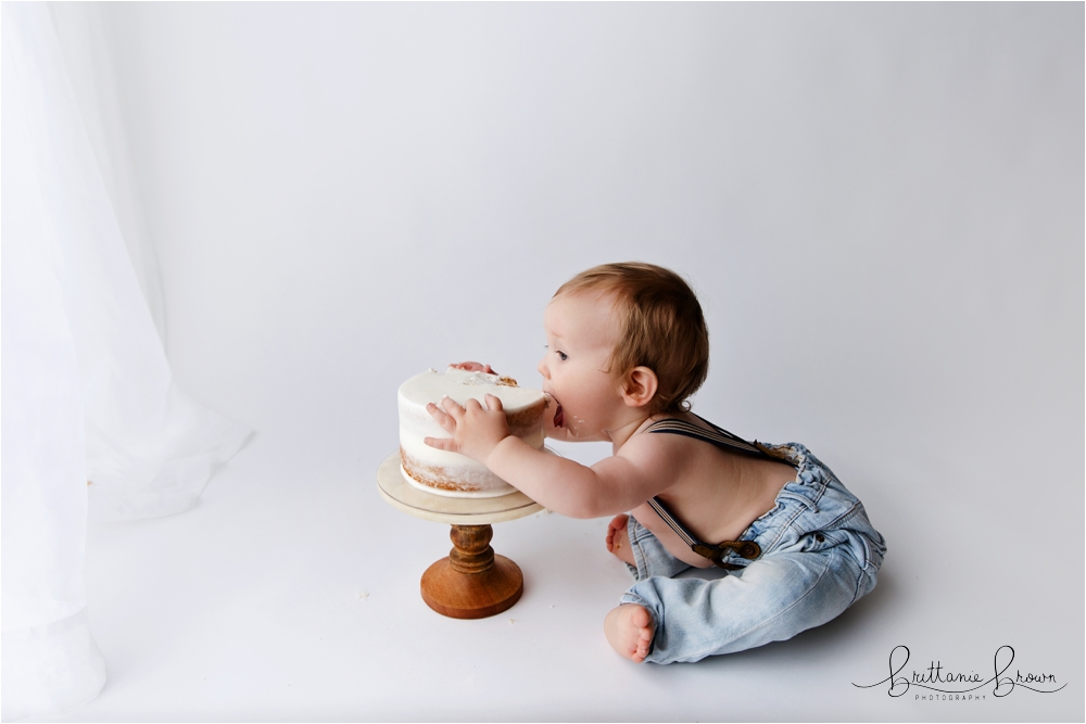 One-year-old Bennett going headfirst into his cake, mouth wide open during his cake smash session